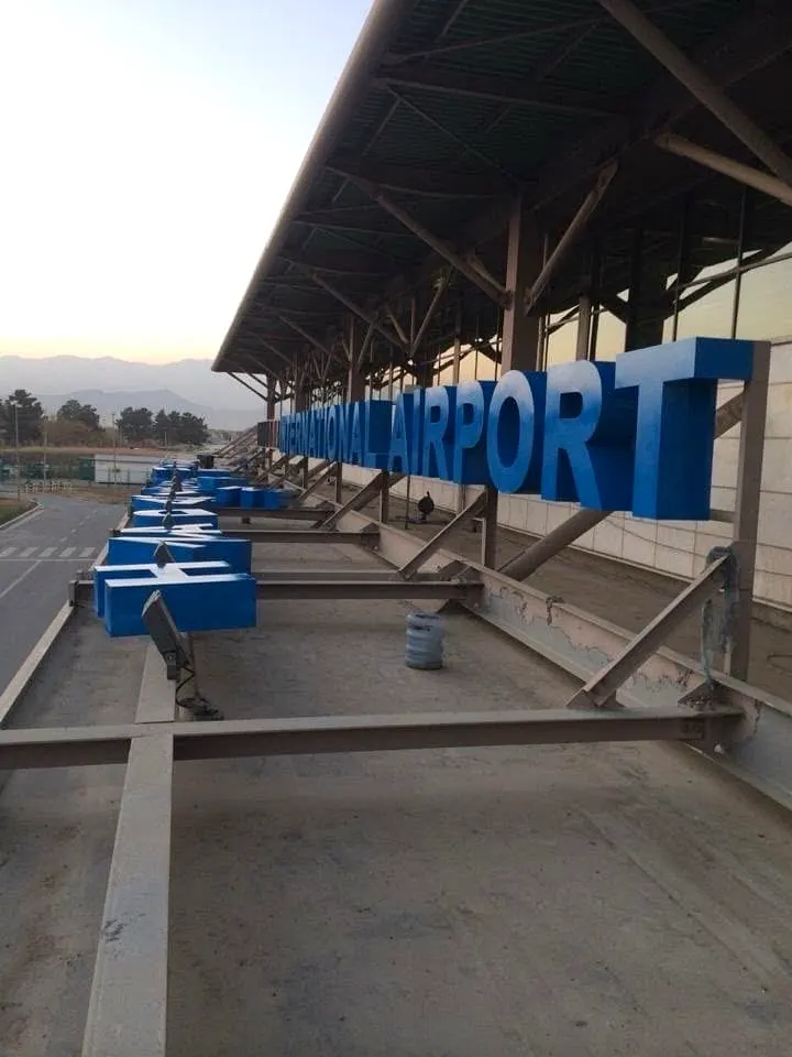Site photo taken on the terminal roof: the same blue letters on their steel frame, running along the canopy edge.