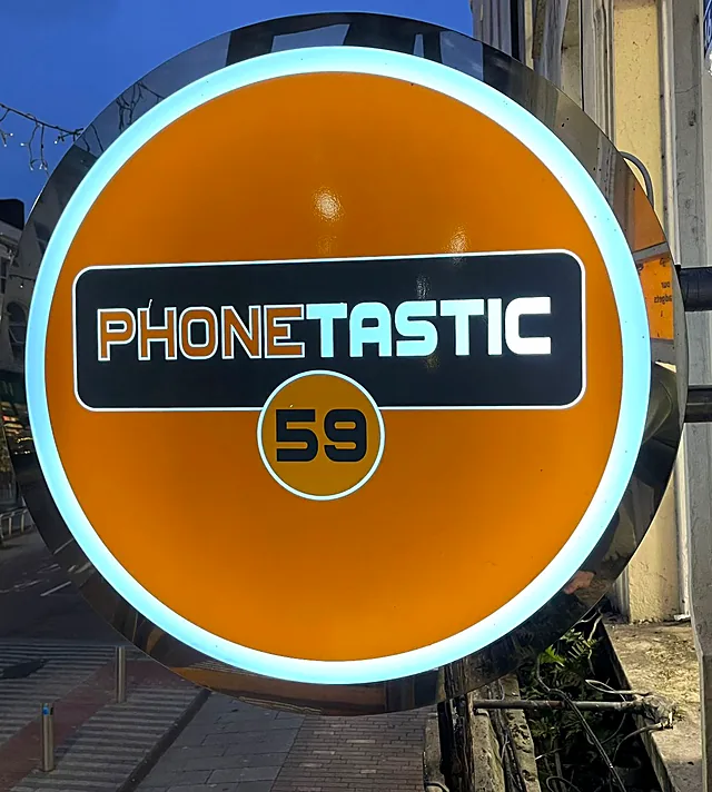 Round orange Phonetastic projecting light box with a glowing white edge, on a bracket above a Cork street at dusk.