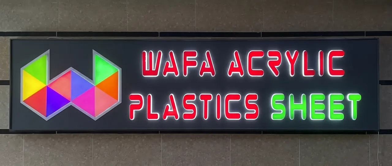 Dark fascia sign with a multicoloured triangle W logo and LED-lit red and green letters reading Wafa Acrylic Plastics Sheet.